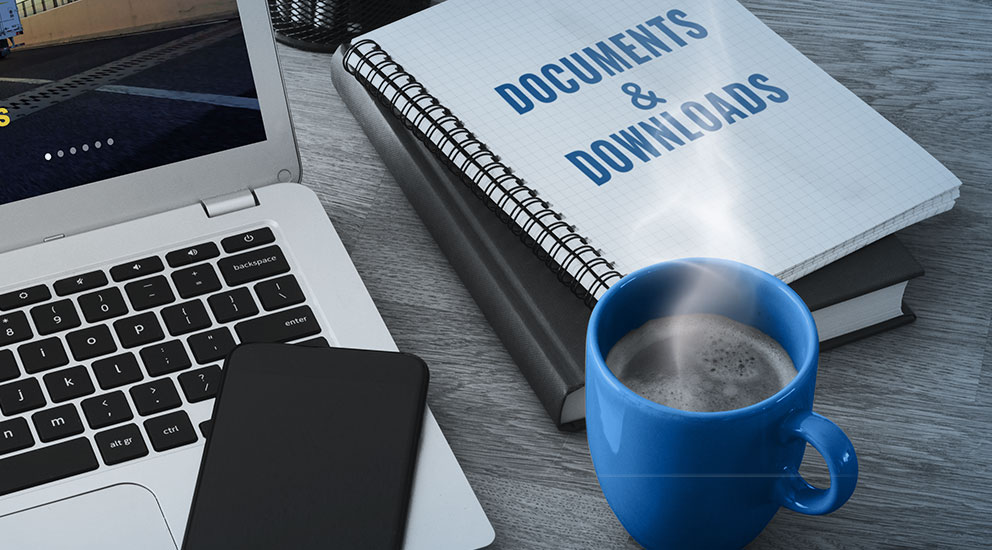 Laptop with Polaris website on screen, smartphone with blank screen sitting on it with coffee and notebook beside it 