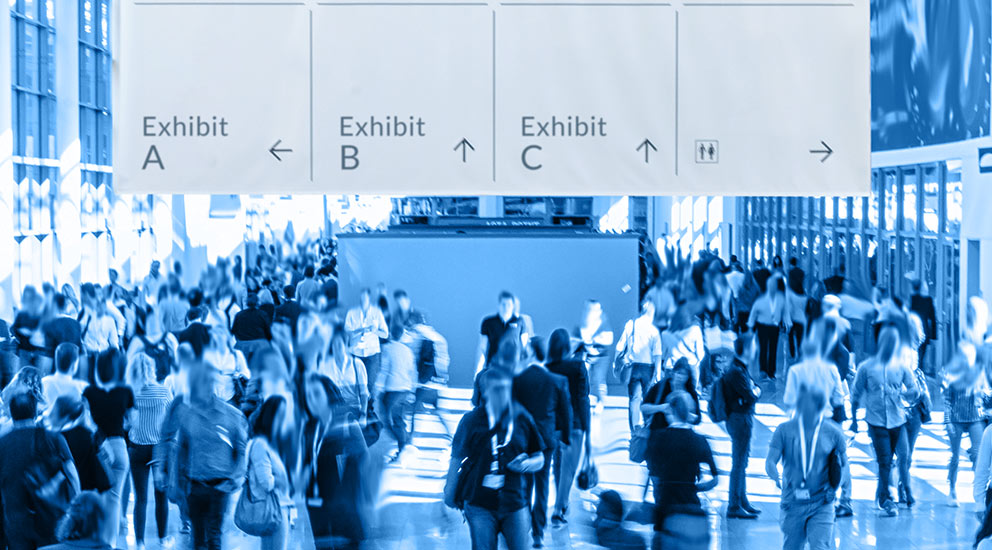 Crowd of people attending trade show with signs point to various exhibits