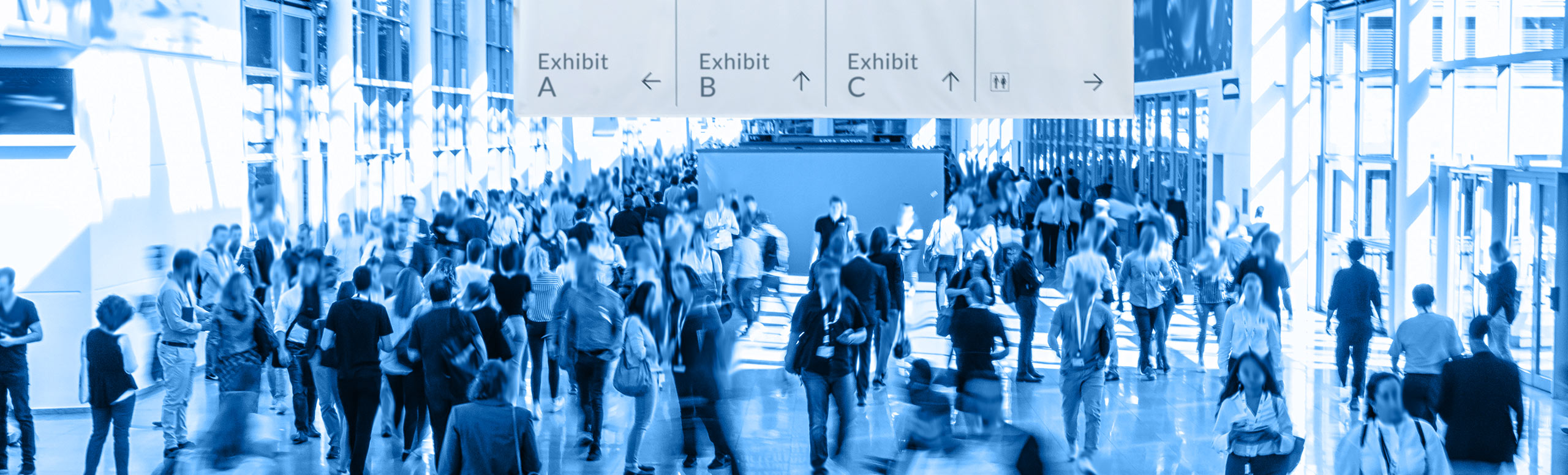 Crowd of people attending trade show with signs point to various exhibits