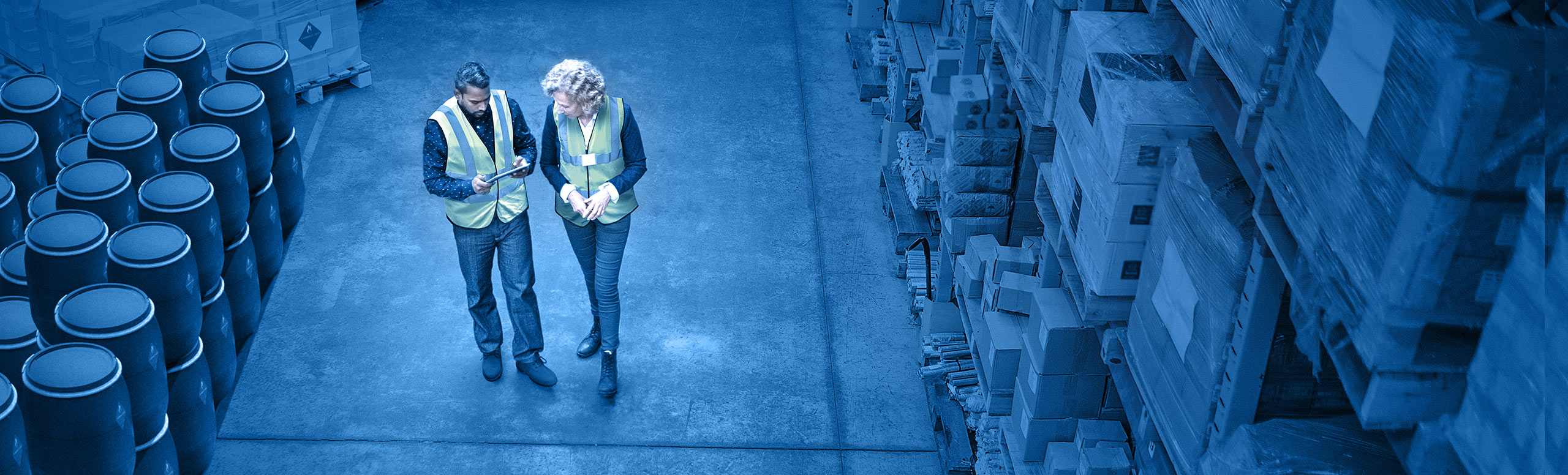Interior of warehouse with two staff walking and reviewing warehouse management system